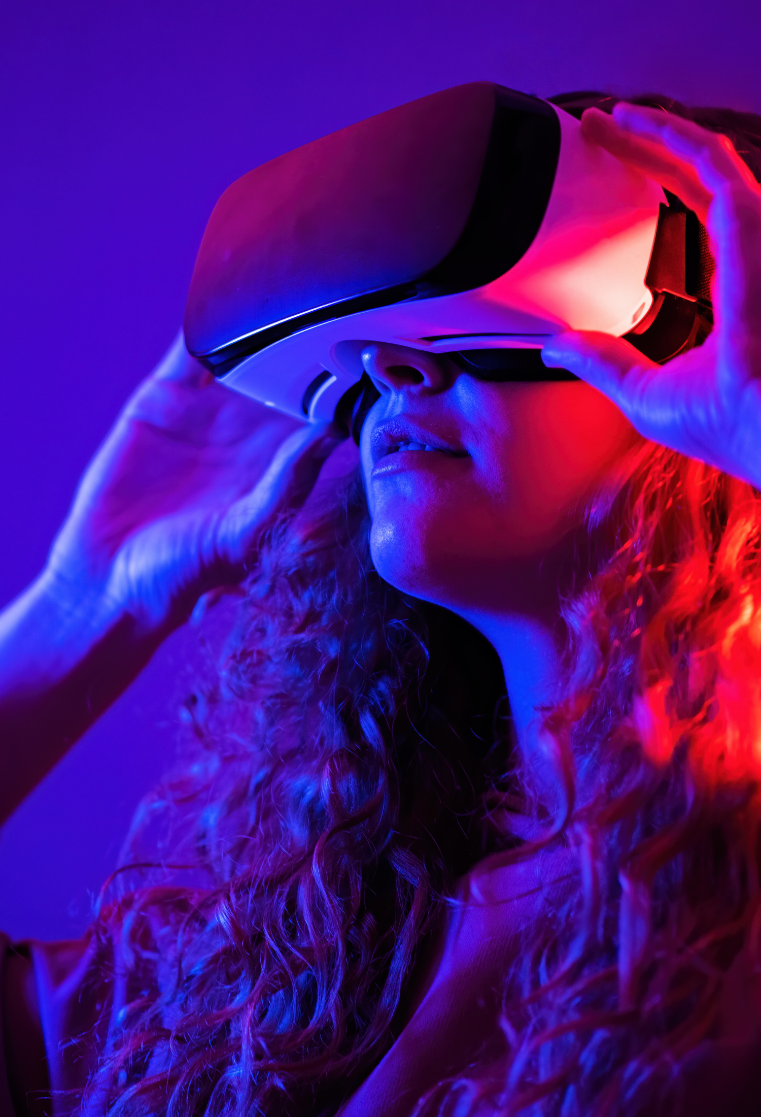 A young girl holds a VR headset to her face, lit in blue and red