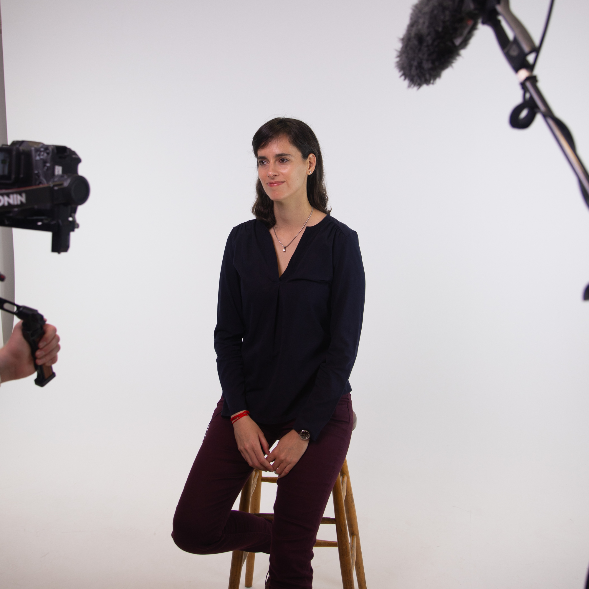 Carissa Veliz, sat on a stool in the middle of a photography studio, looks towards the cameraman