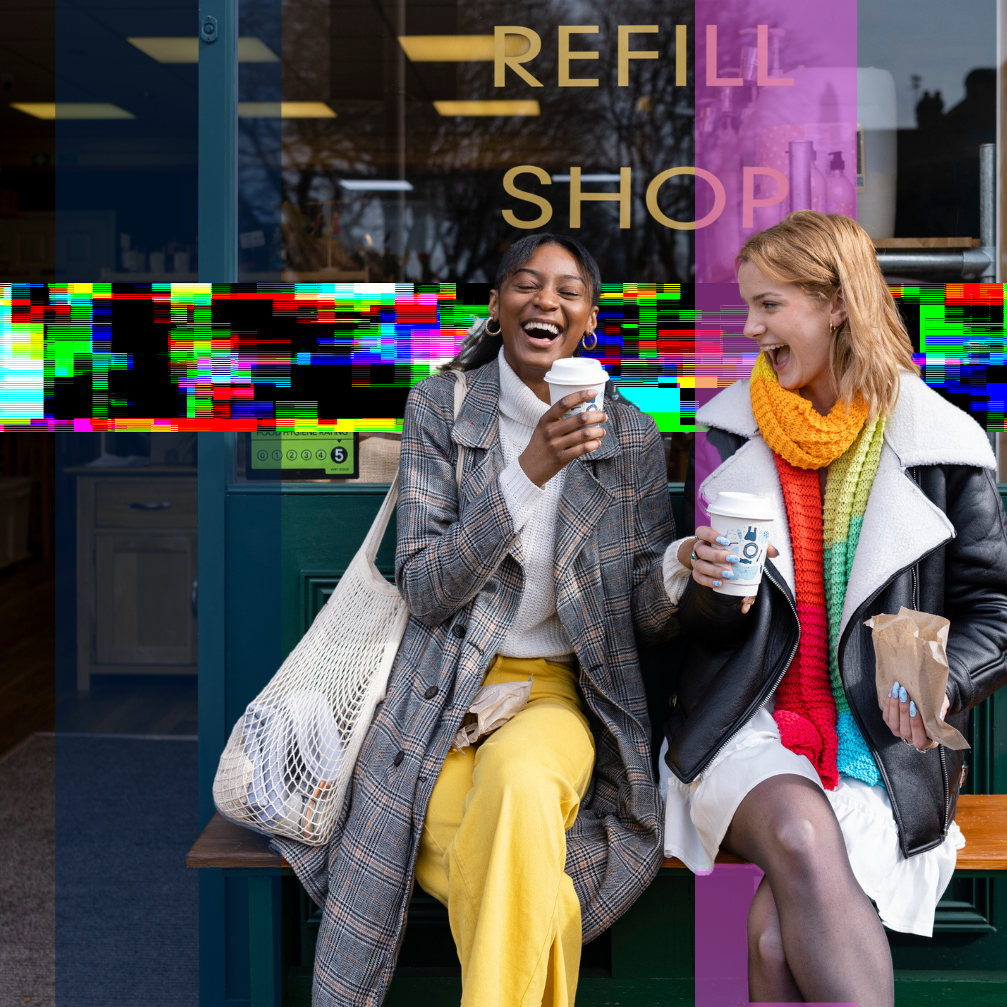 Two women laughing and holding coffee cups outside of a cafe