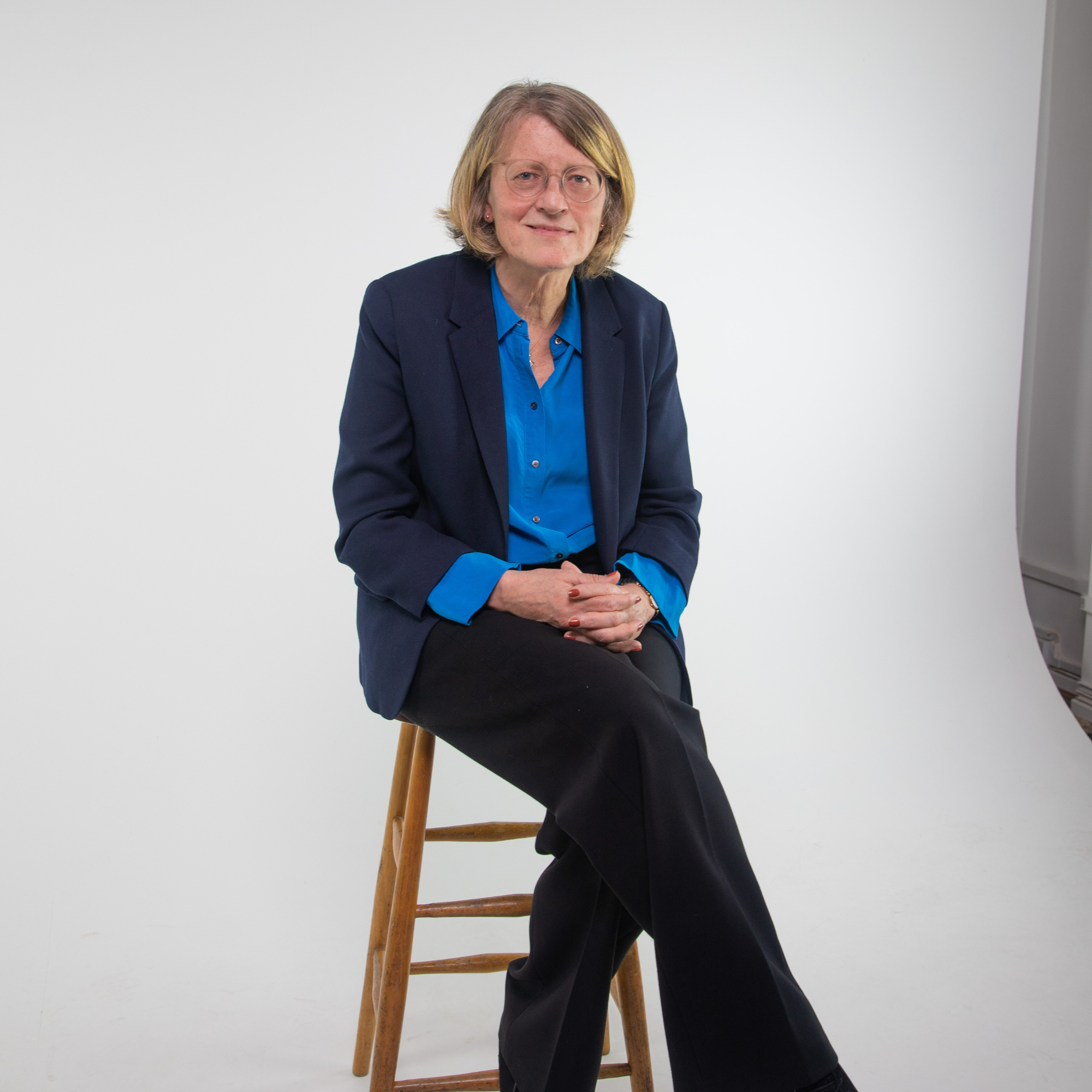 Professor Helen Margetts sits on a stool in the middle of a photography studio and smiles at the camera