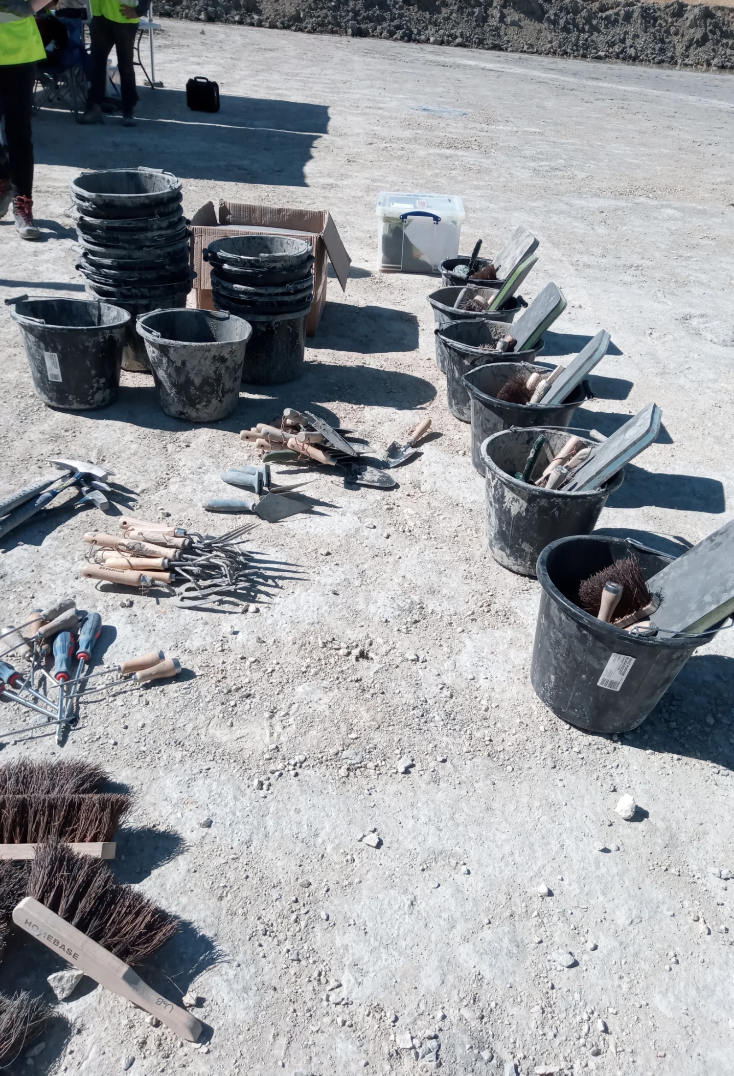 A line of buckets filled with kneeling pads, brushes and shovels on the ground at a quarry.