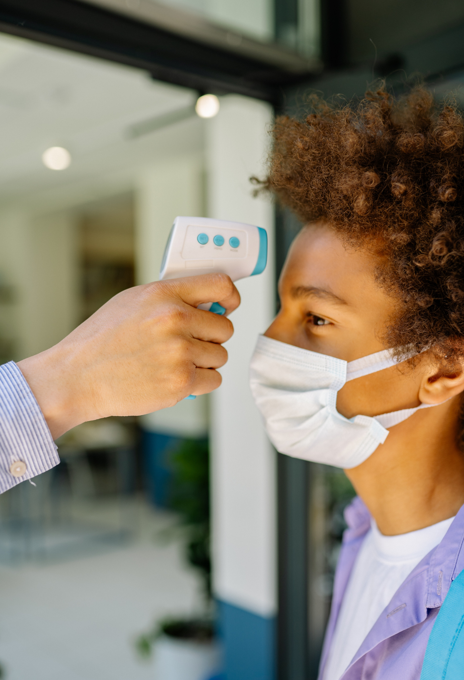 A child wearing a face mask has their head temperature scanned