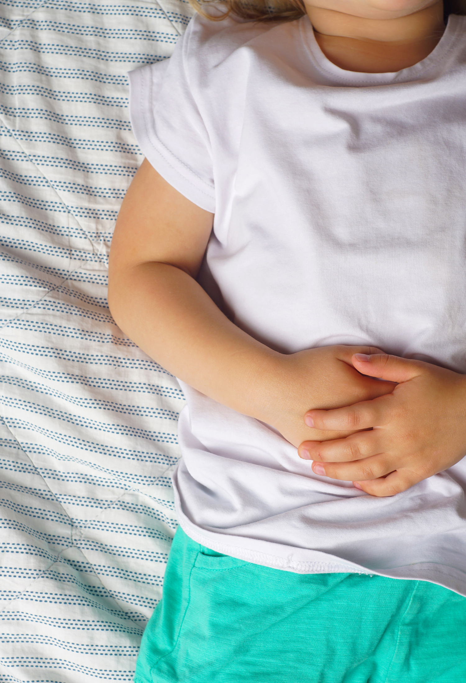 A young child holds their hands together on the stomach while lying down