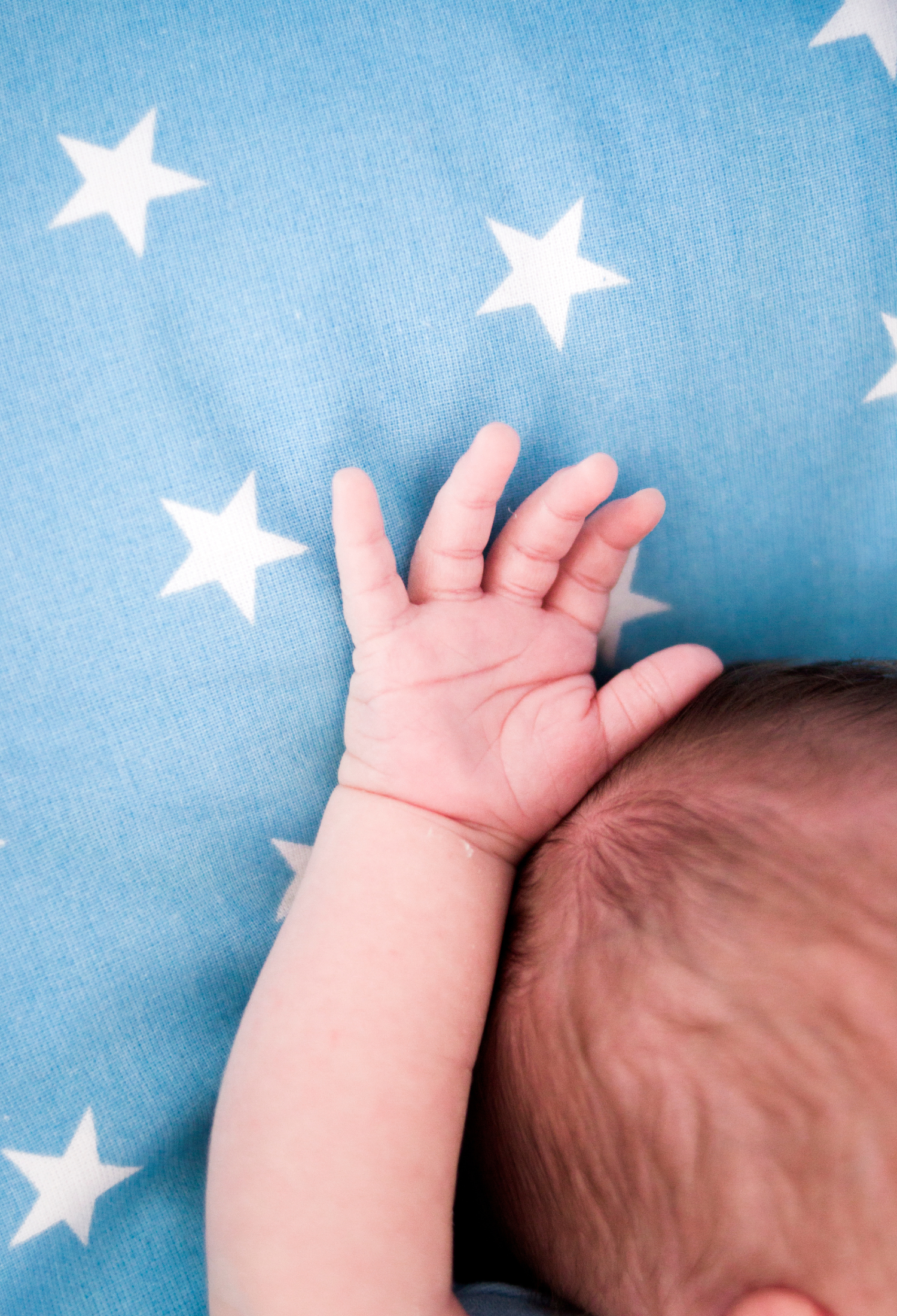 A newborn baby holds its hands up on a starry blanket