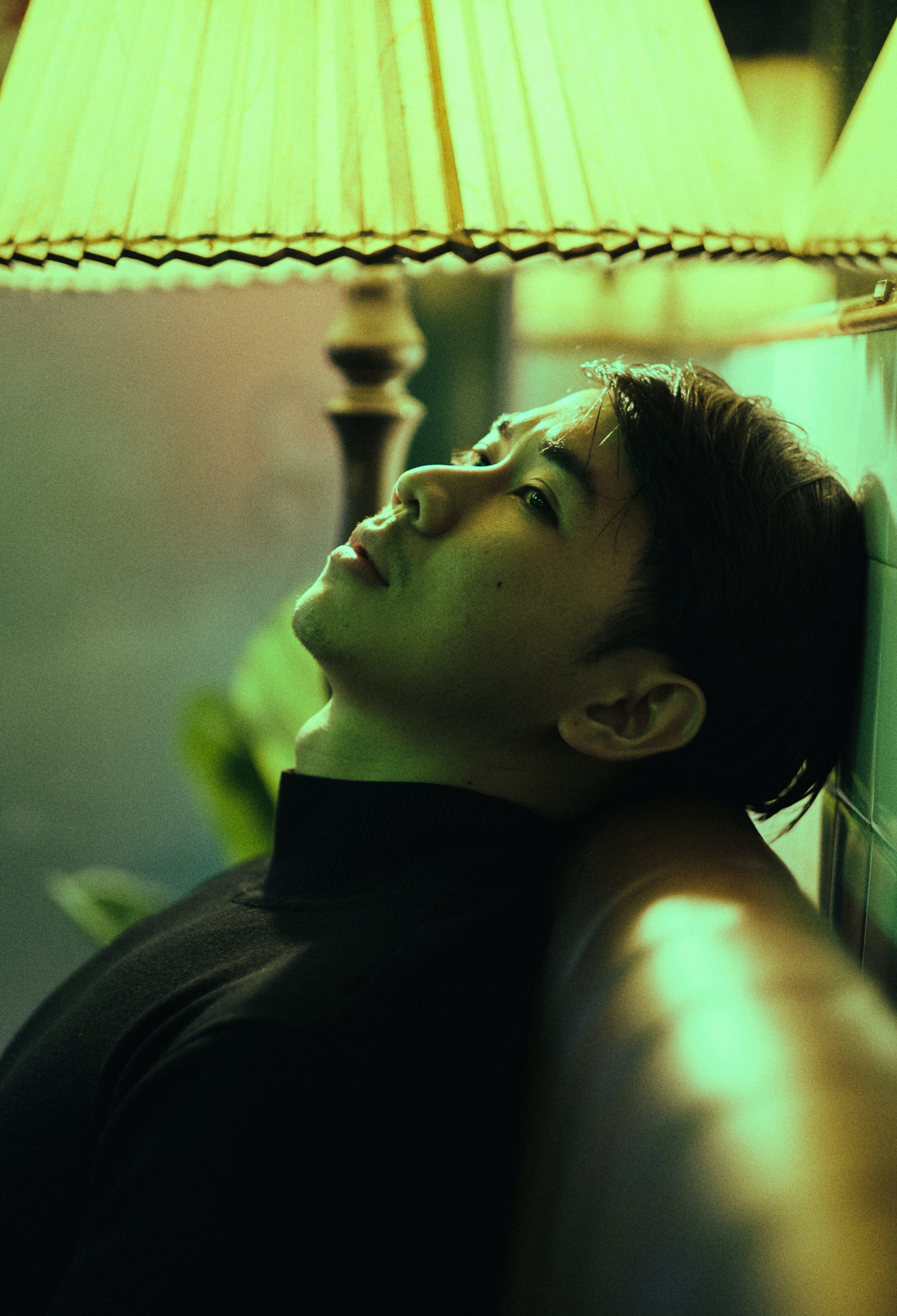 A young person leans their head against a wall, lit by fluorescent light