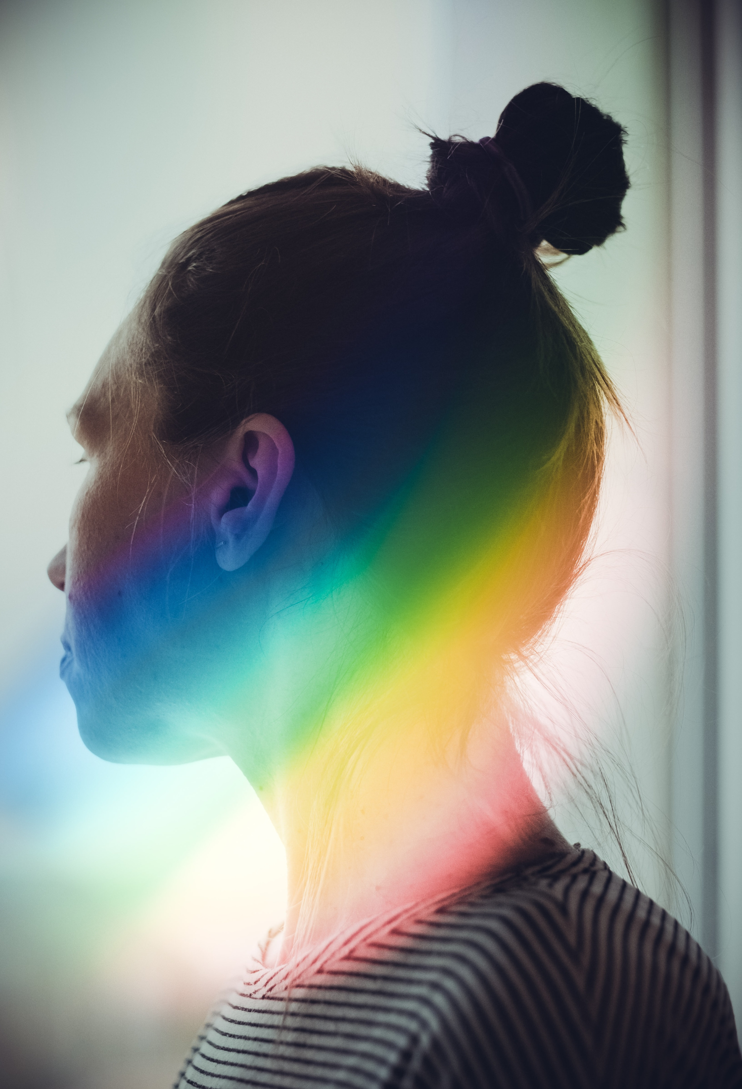 A young person looks away from the camera, with a rainbow lens flare