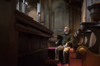 Dr Pegram Harrison sits in some church pews.