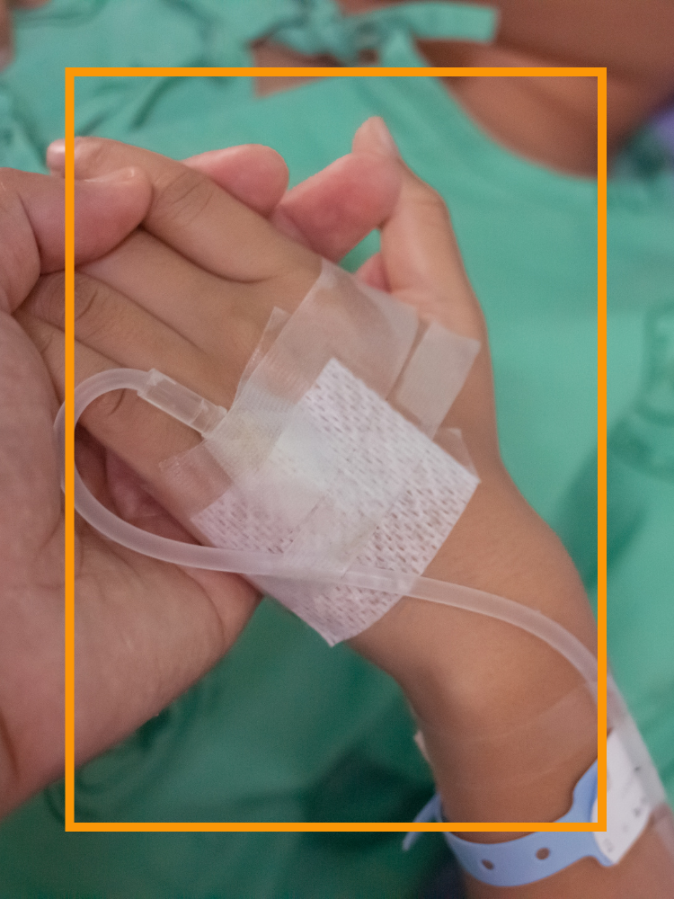 An adult hand holding a child's hand with an IV inserted