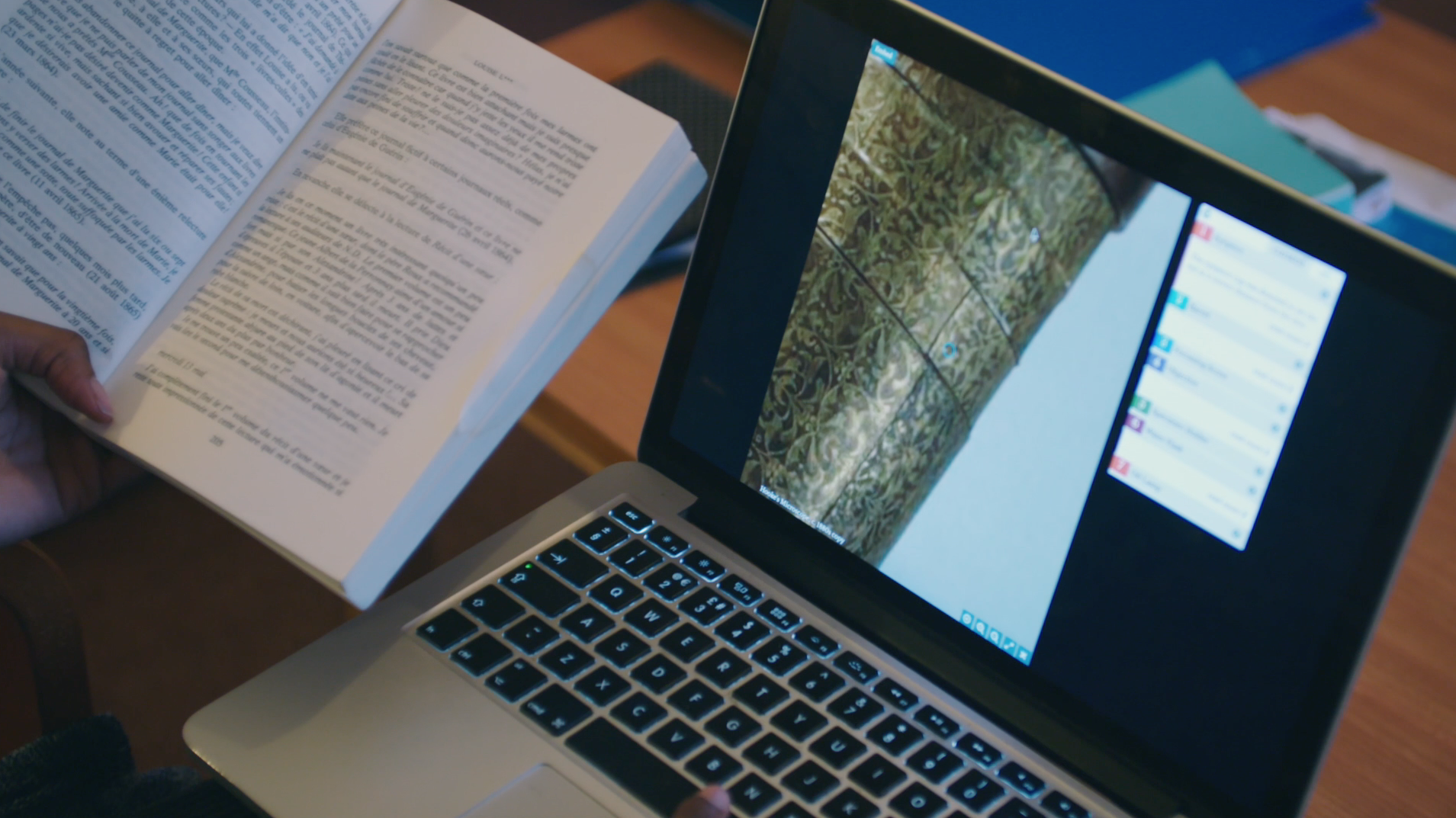 A laptop showing a museum object and annotations, with a book alongside