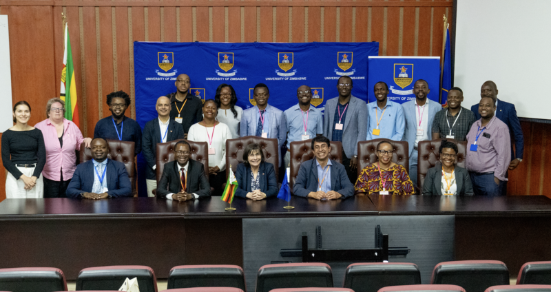 A large group of people sit and stand in front a backdrop reading 'University of Zimbabwe'