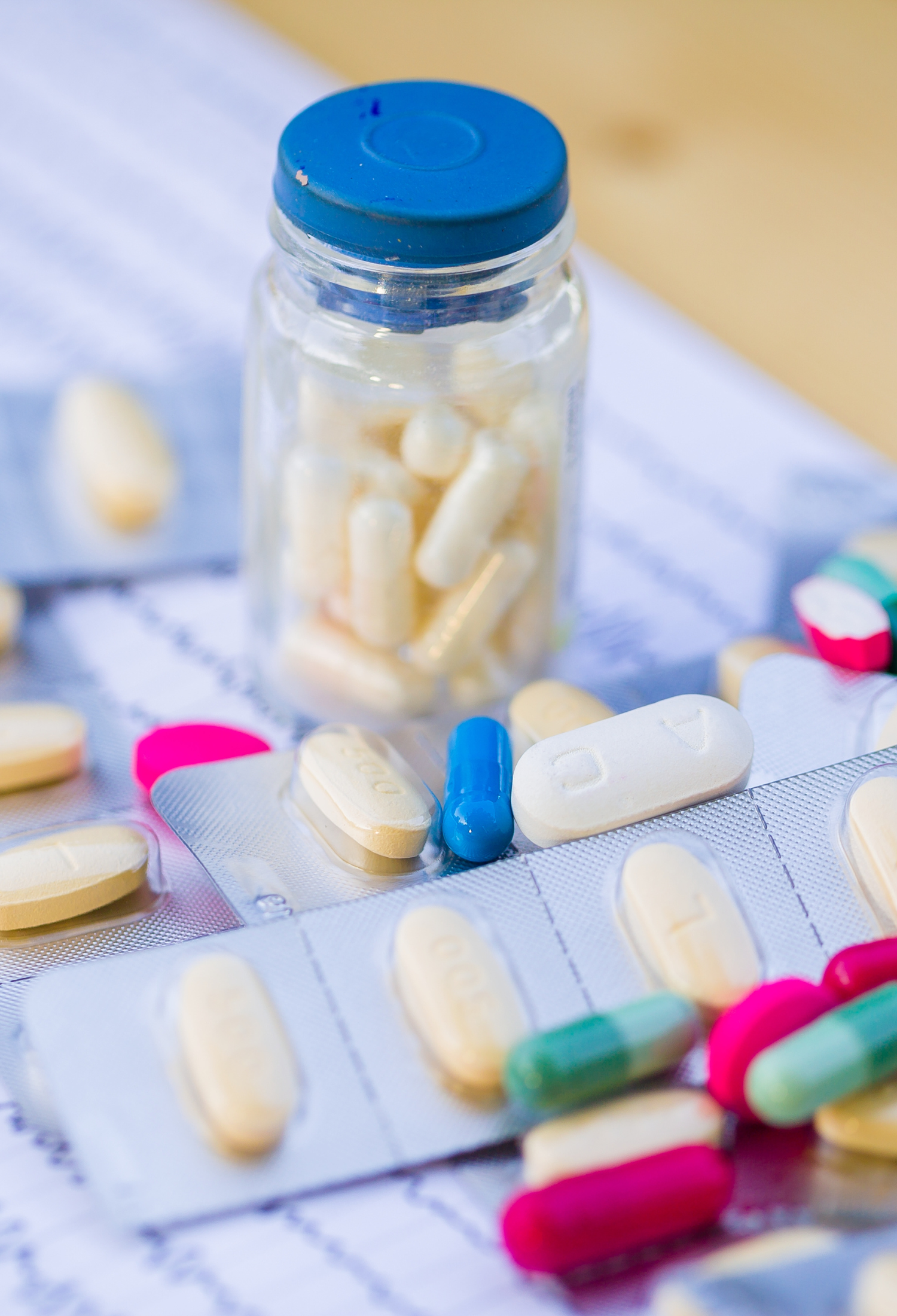 A vial of tablets sits on a table surrounded by blister packs of other tablets