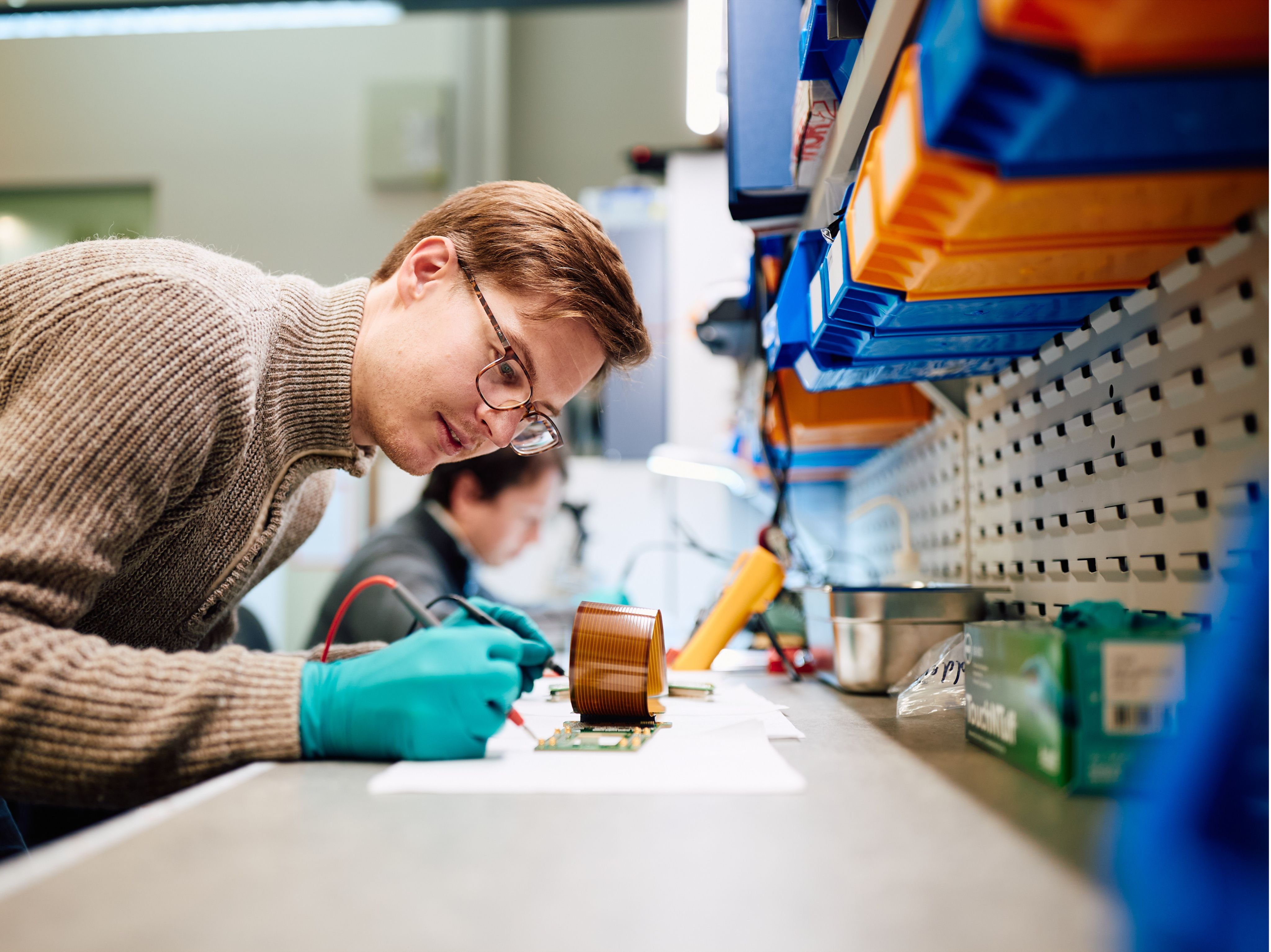 A young white man wearing latex gloves works on parts of a quantum computer on a lab bench.