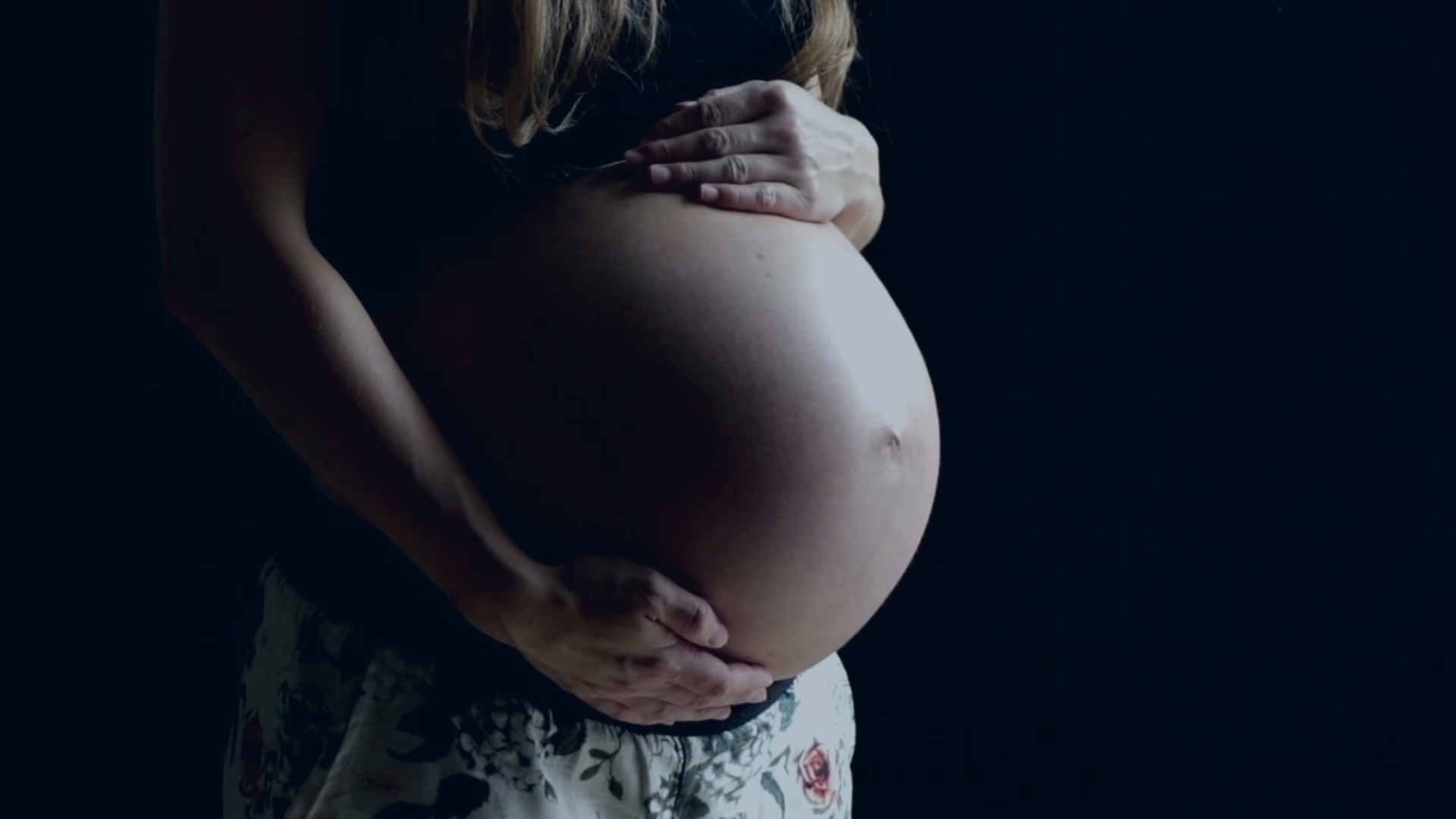 A pregnant woman cradles her baby bump