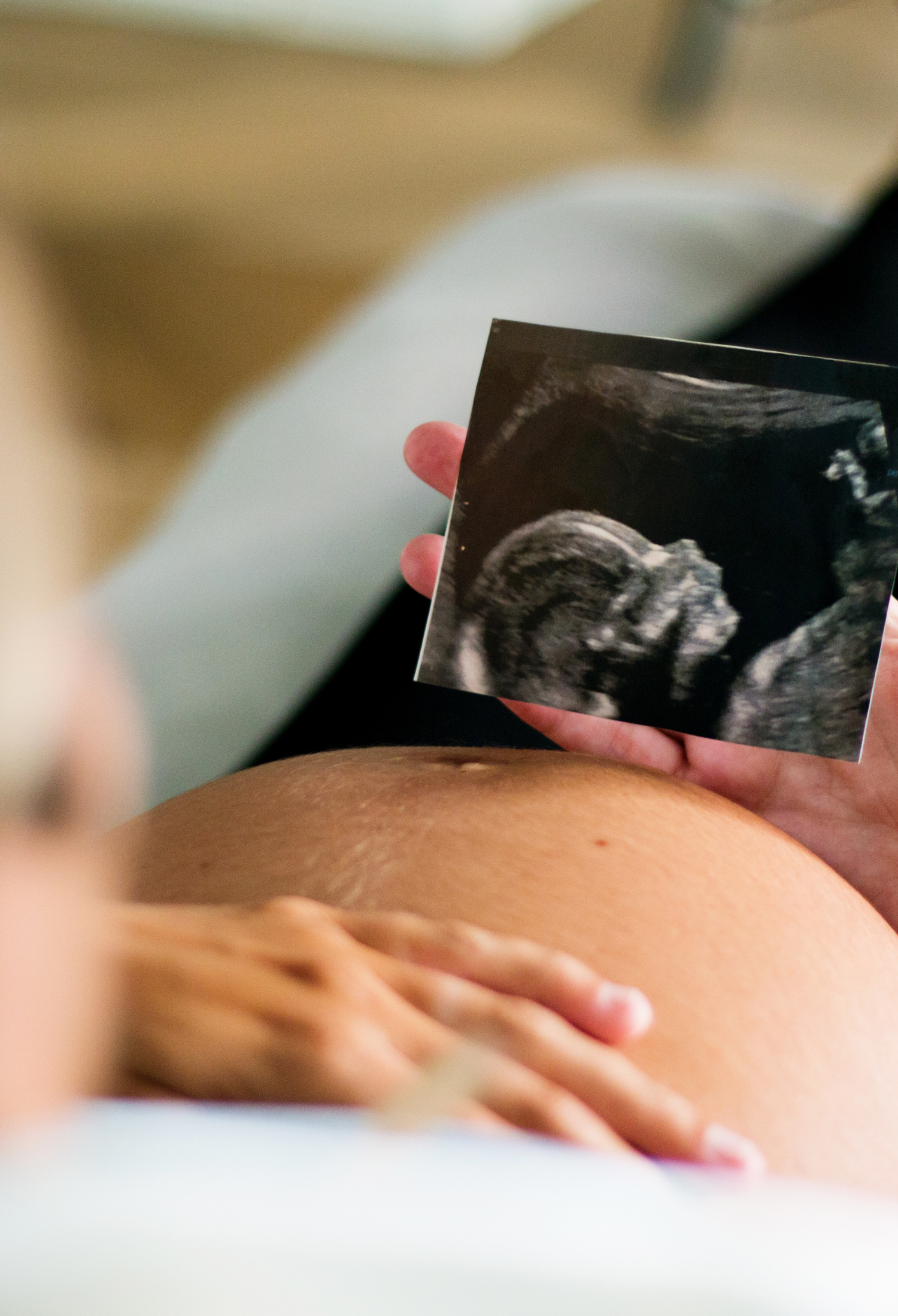 Someone holding an ulstrasound image above a pregnant belly