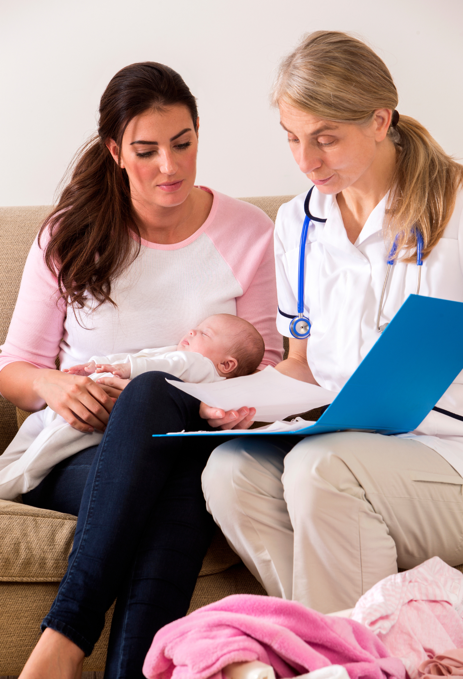 A woman holding a baby and talking to another woman with a stethoscope