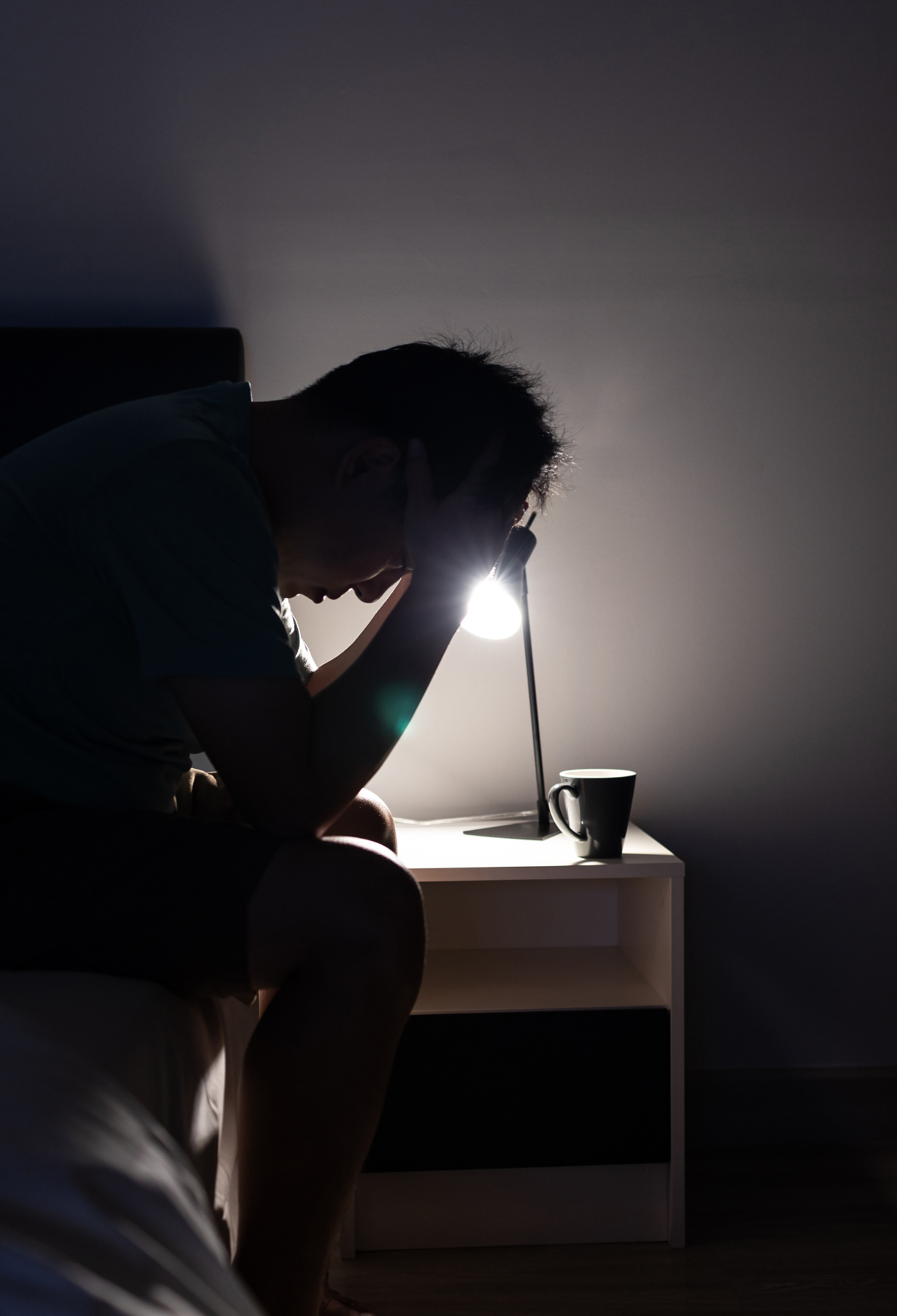 A silhouette of someone sitting up in bed next with their head in their hands