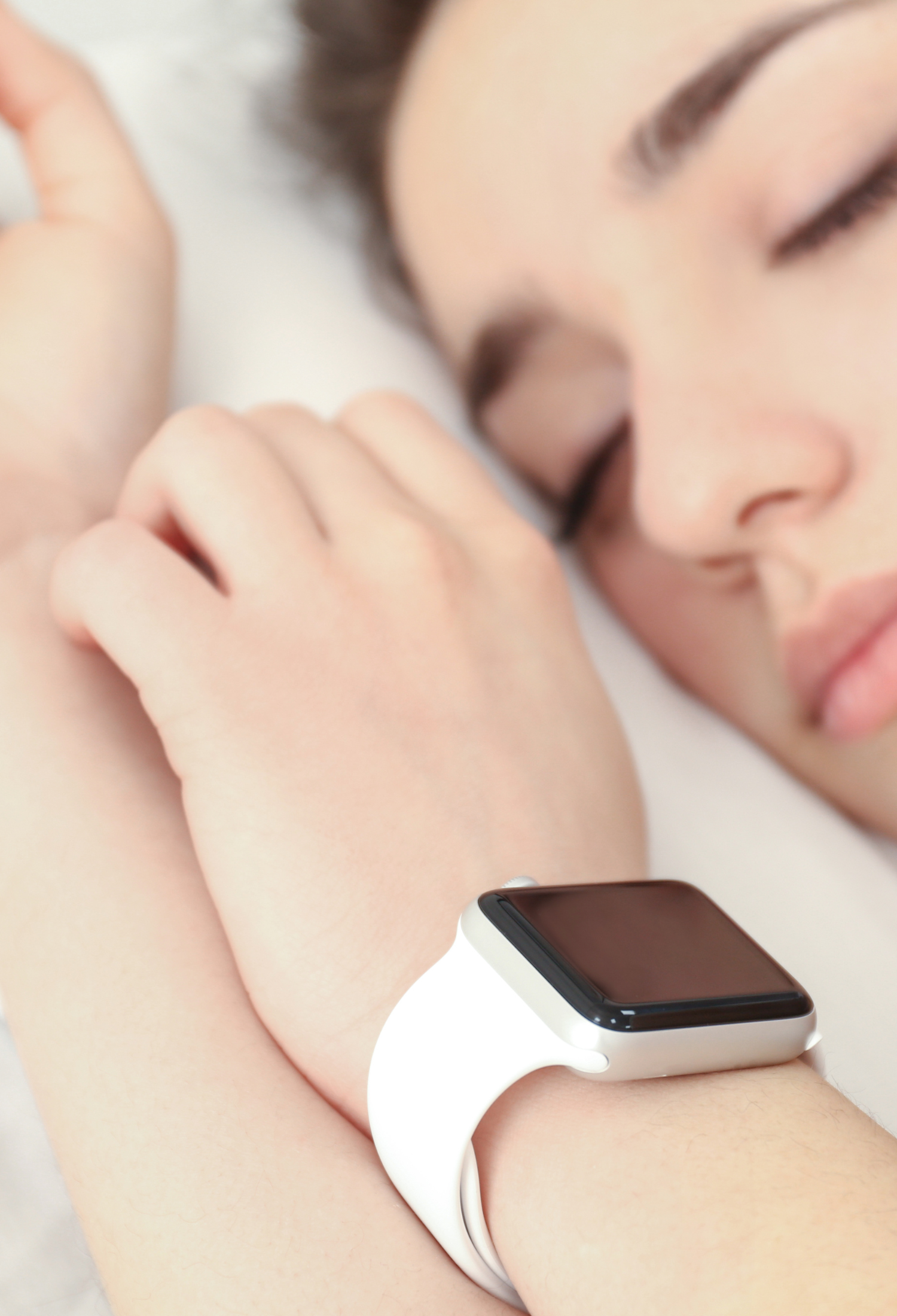 A woman sleeps with a sleep tracking watch on her wrist