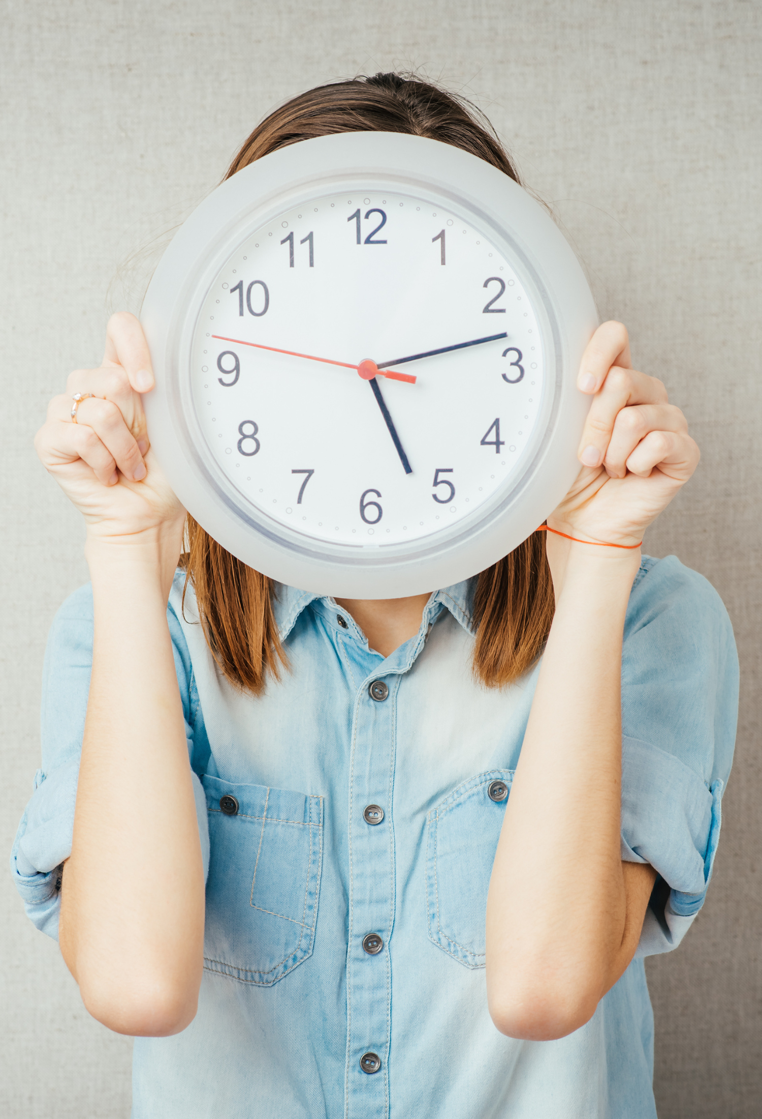 A woman holds a clock over her face