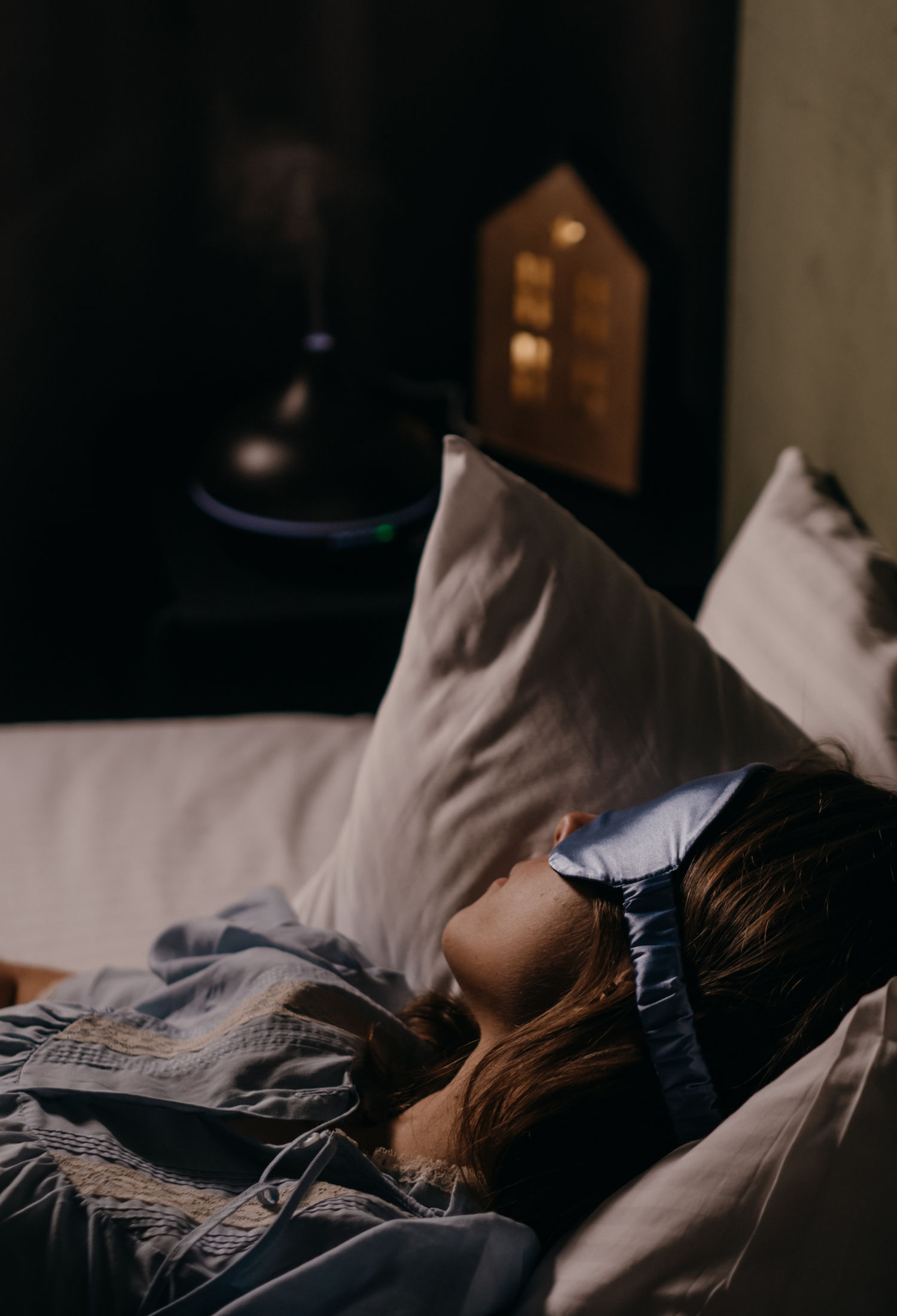 A person sleeps in bed, propped up on pillows with an eye mask on