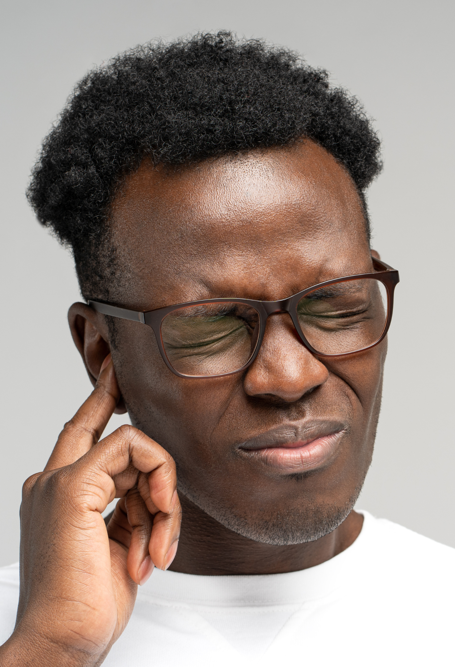 A man holds his finger to his ear and winces, likely in pain from tinnitus
