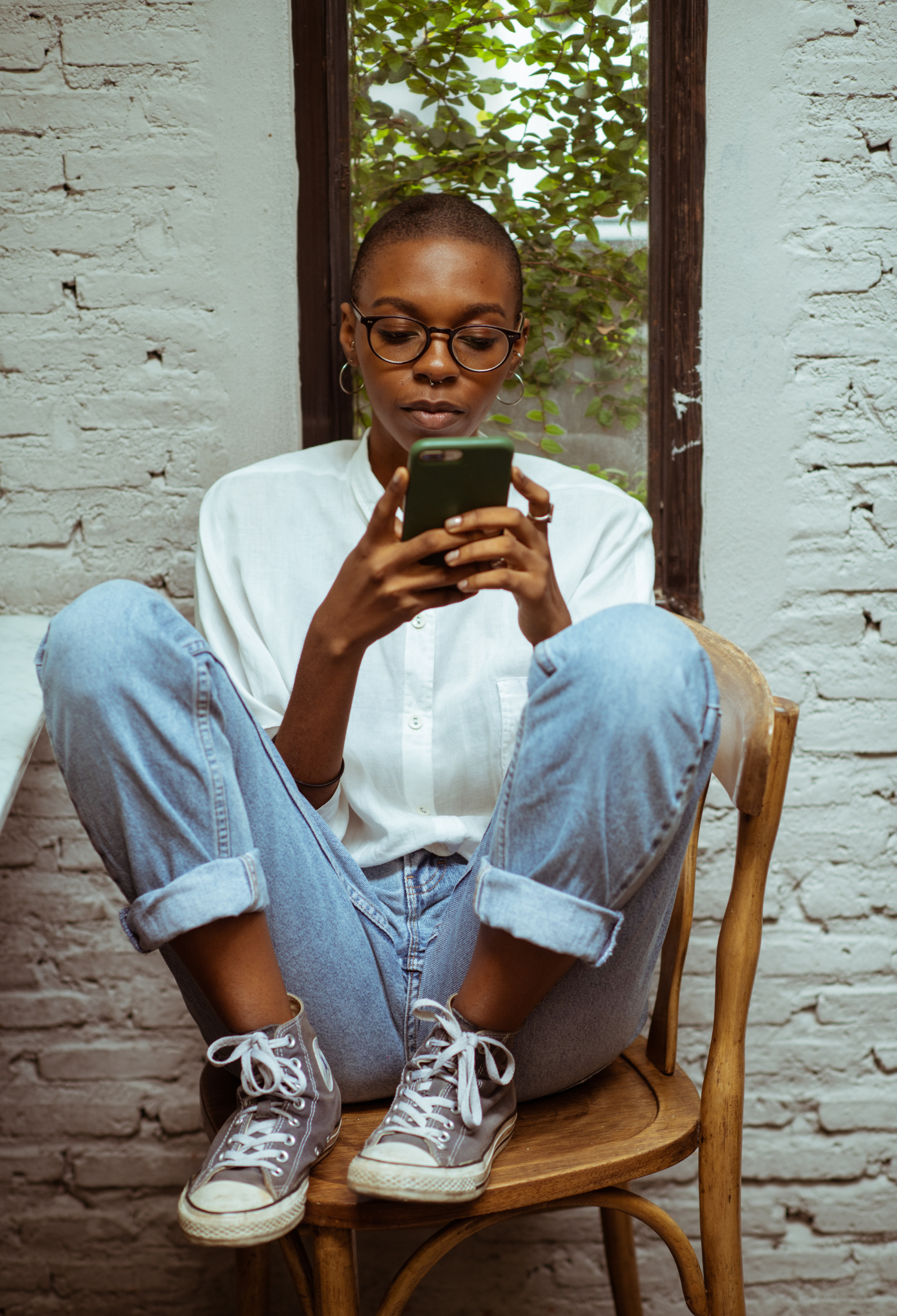 A young woman sits on a chair with her legs crossed holding a mobile phone