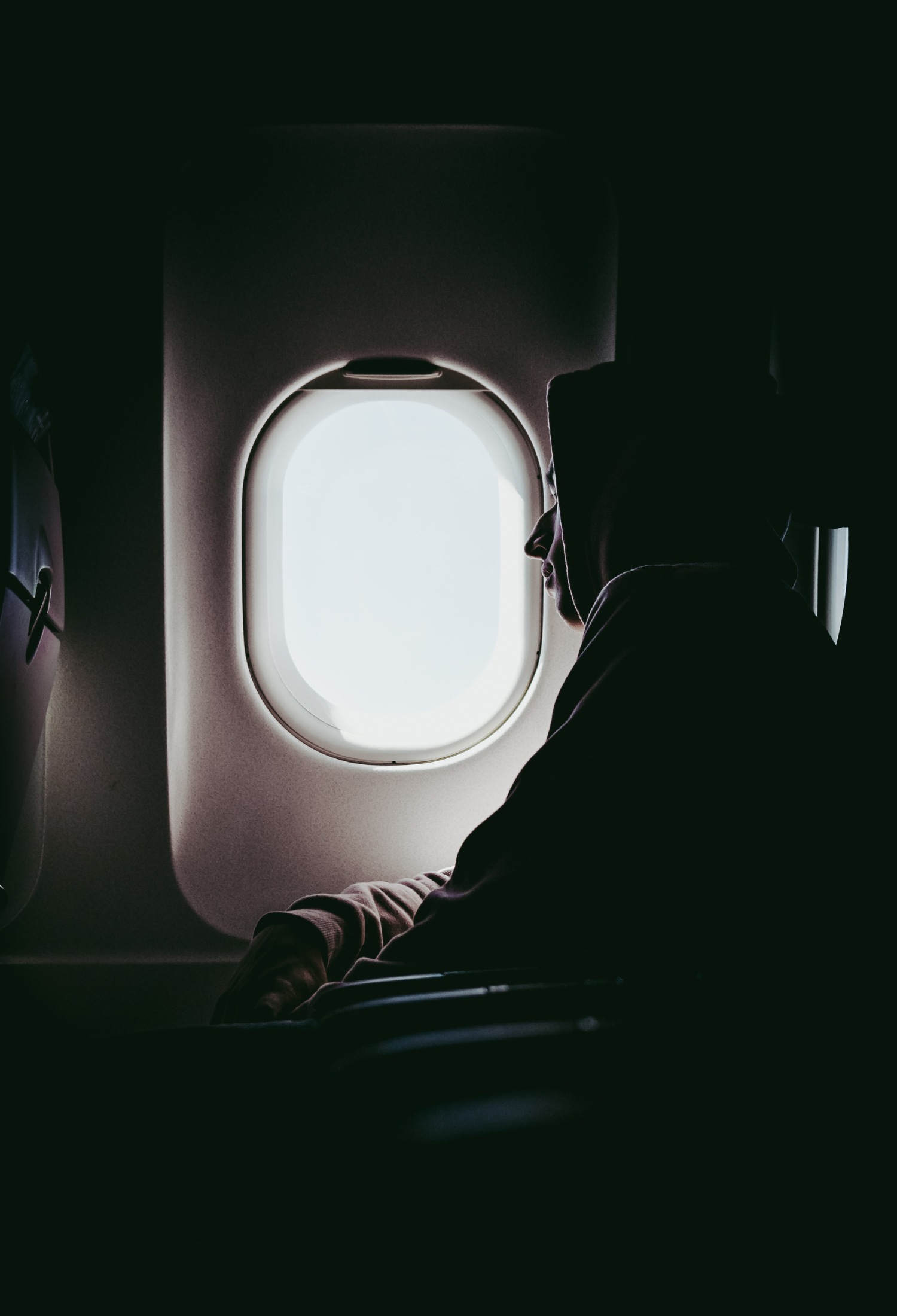 Someone wearing a hoodie leans on an aeroplane window